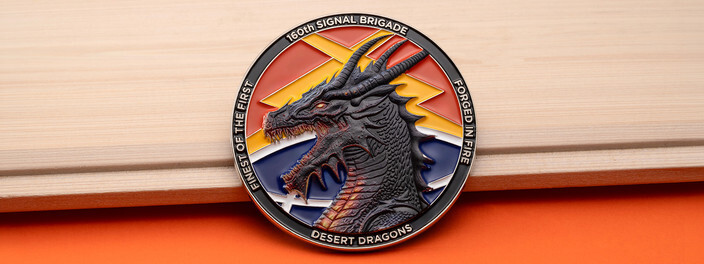 Round coin with a sculpted dark gray dragon head over orange, yellow and blue lightning, ringed in black, on light wood