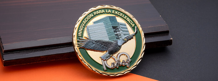 Round gold and green coin with a printed glass office tower and a sculpted eagle in flight, on dark wood
