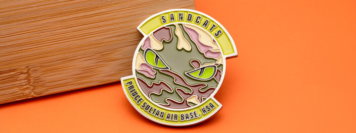 Silver cutout coin of green cat eyes in desert camouflage, for the Sandcats at Prince Sultan Air Base