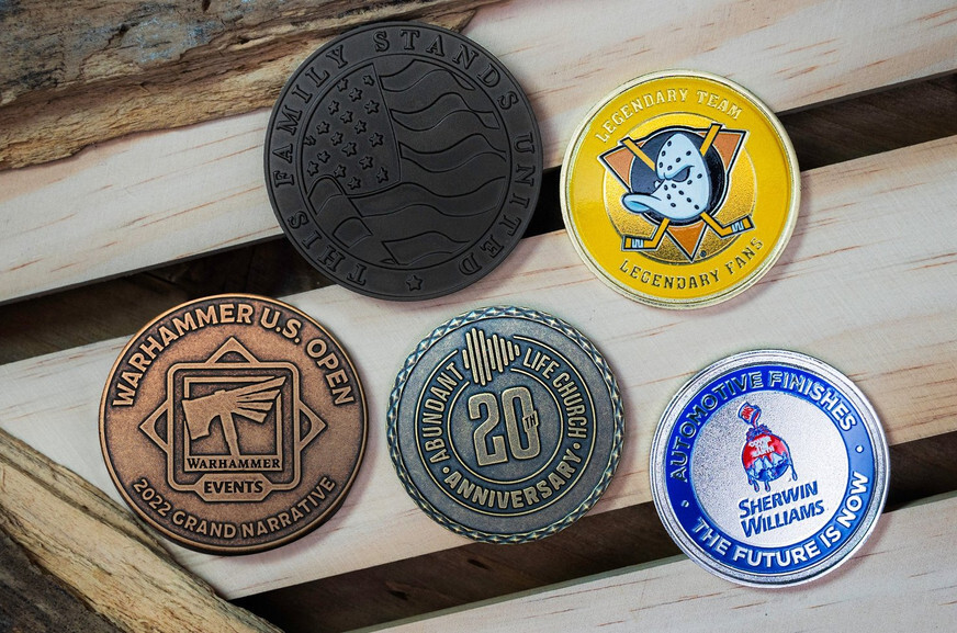 Five round coins in black, gold, copper, antique brass and silver with blue enamel, on light wooden slats