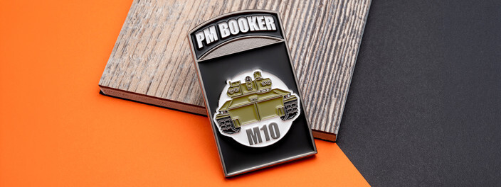 Black rectangular coin with an olive green M10 Booker armored vehicle under a name tab, on gray wood and orange