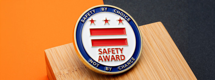 Blue and white safety award coin with three red stars and two red bars, on light wood and orange paper