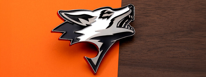Black and silver wolf head shaped coin with an opener cut into its open jaw, on orange paper and dark wood