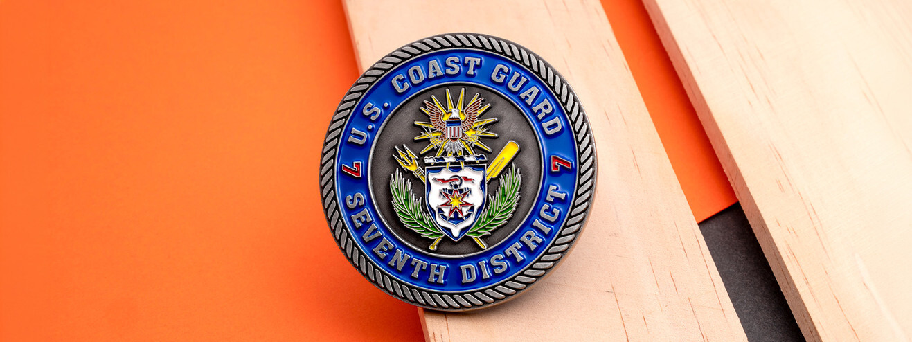 Antique silver Coast Guard Seventh District coin with the unit's crest inside a blue enamel ring, on orange paper and wood