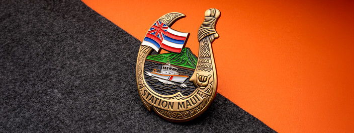 Antique gold fishhook-shaped Station Maui coin with the Hawaii flag, a green mountain and a response boat