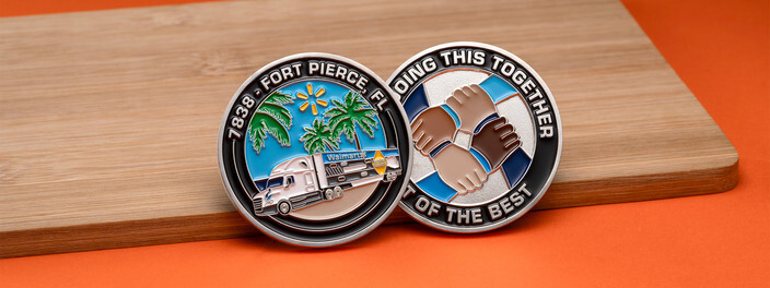Two silver coins, one with palm trees and a semi truck, one with four linked hands in a circle