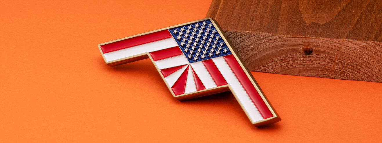 Stealth bomber shaped coin in red, white and blue enamel with American flag stars and stripes, on orange paper and wood