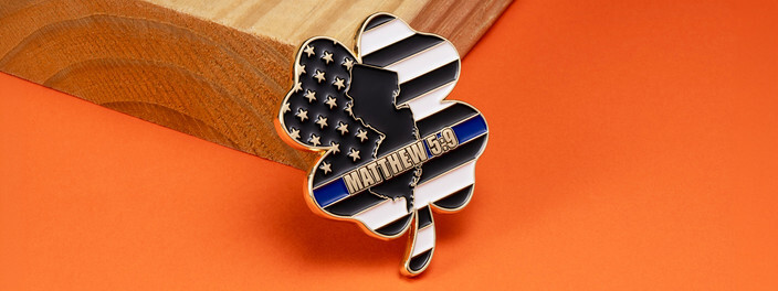 Shamrock shaped coin with a black and white flag, a state outline and a thin blue line banner, on orange paper