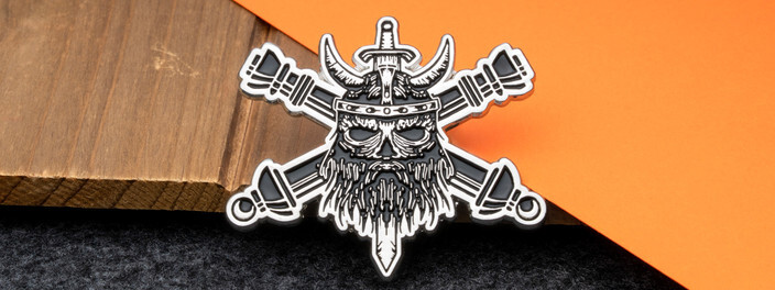 Silver cutout coin of a horned viking skull over crossed swords, on dark wood and orange paper