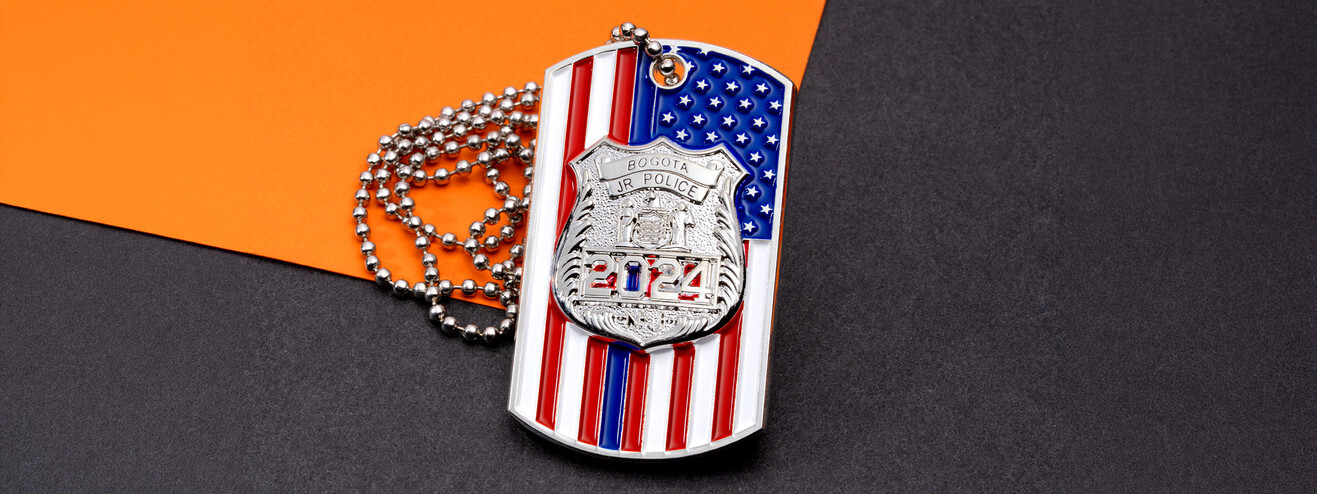 Red, white and blue flag dog tag with a silver junior police badge and a ball chain, on orange and black