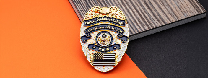 Gold badge shaped police reserve class coin with an eagle on top and a small American flag, on orange paper and gray wood