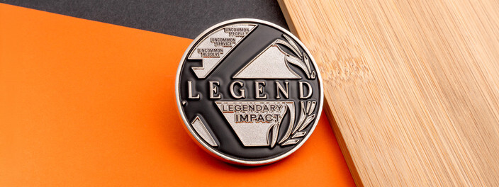 Silver and black Legend coin reading Legendary Impact beside a laurel branch, on orange paper and bamboo