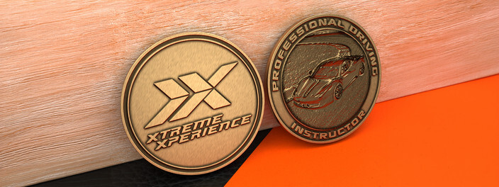 Two antique bronze coins, one with a double chevron logo and one with a sports car on a racetrack
