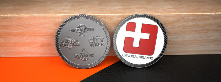 Two silver theme park coins, one engraved with park logos and one with a red logo on white enamel