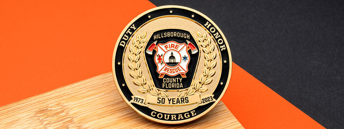 Gold fire rescue coin marking 50 years of service, with a laurel wreath and a Maltese cross, on a wooden board