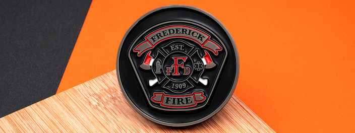 Black round coin with a red Maltese cross and a fire truck, on an orange and wood background