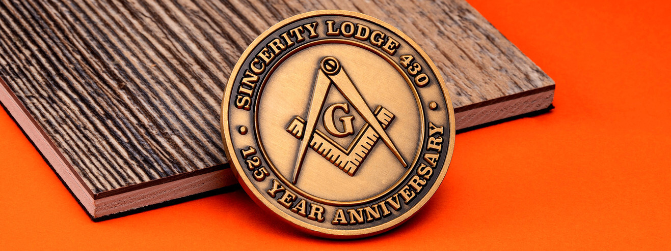 Antique bronze lodge anniversary coin with the square and compasses and the letter G, on wood and orange