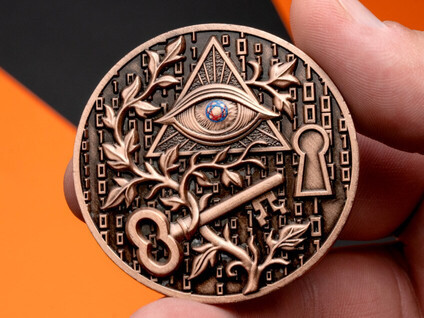 Copper all-seeing-eye and key challenge coin held between two fingers
