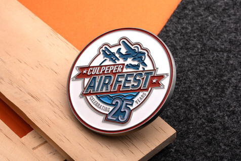 White, red and blue enamel coin for an air fest's 25th anniversary, with vintage planes, resting on a wood block