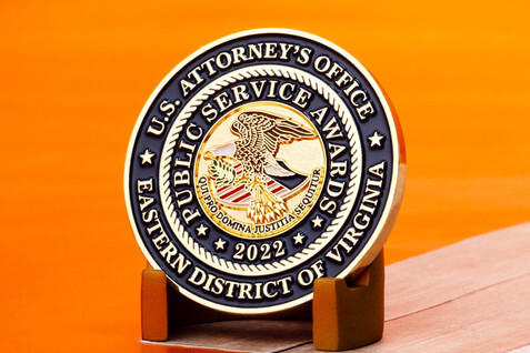 Gold coin with the seal of a United States Attorney's Office on a wood block
