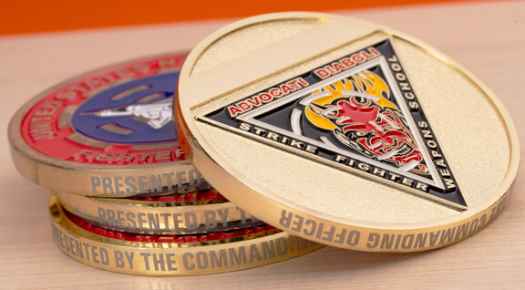 Stack of gold challenge coins on a table, the top one showing a triangle emblem