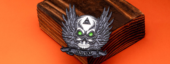 Black winged skull coin with glowing green eyes over a Bravo banner, on a dark wooden block
