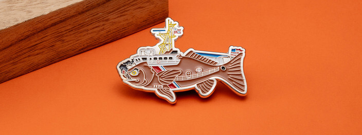 Silver cutout coin of a scowling fish carrying a ship's mast and deckhouse, with hull number 1125