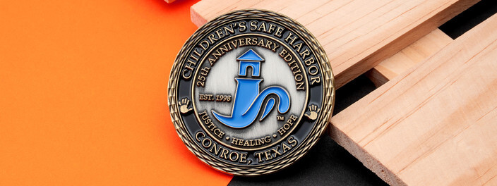 Antique bronze 25th anniversary coin with a blue lighthouse emblem for a children's advocacy center, on light wood
