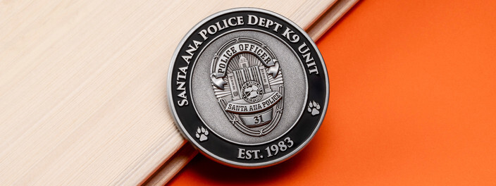 Antique silver K9 unit coin with a police officer badge and paw prints, on light wood and orange paper