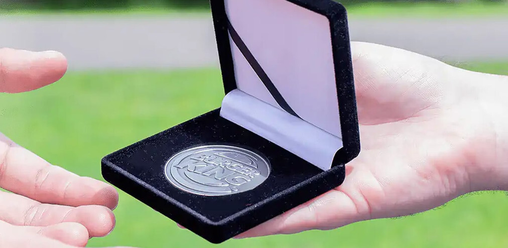 Silver coin in an open black velvet box passed between two hands above green grass