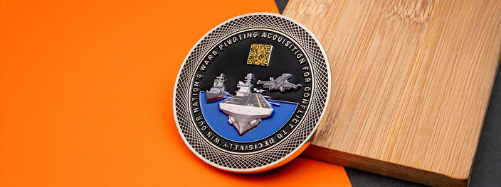 Silver coin with an aircraft carrier, a warship and a jet over blue water, with a small gold QR code above