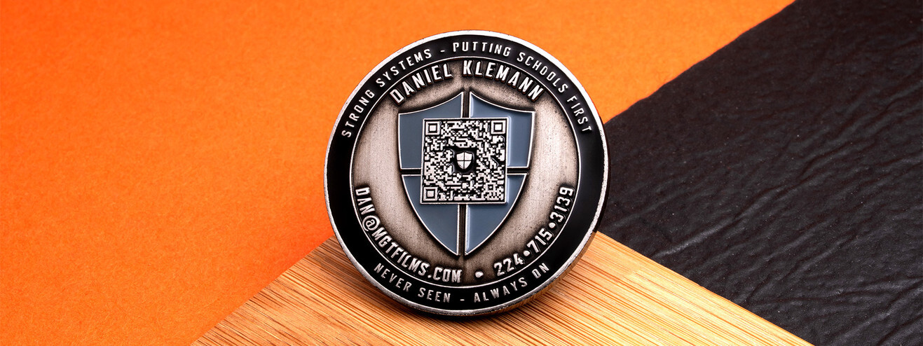 Antique silver coin with a QR code inside a blue shield, ringed by a school security company's motto and contact details