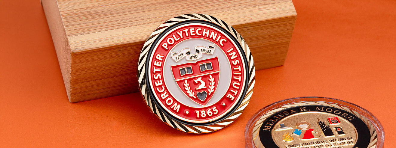 Red and white college seal coin with a twisted gold edge beside a scholarship coin in a clear capsule