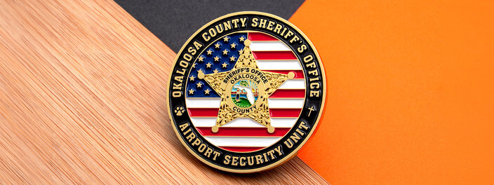 Gold sheriff's star over an American flag on a black rimmed airport security unit coin, on wood and orange paper
