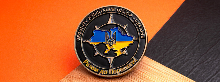 Black security assistance group coin with a compass rose behind a blue and yellow map of Ukraine, on bamboo