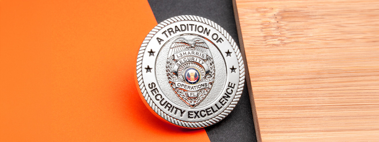 Silver coin with a security officer badge and the words A Tradition of Security Excellence, on wood and orange paper
