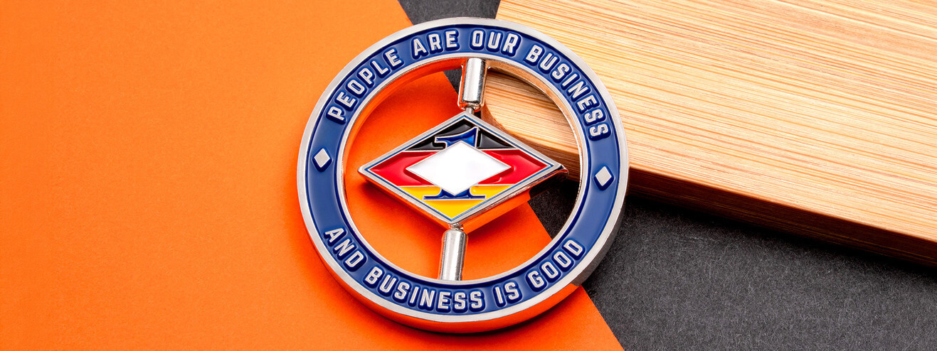 Silver and blue spinner coin with a diamond emblem turning on two posts inside the ring, on orange paper and bamboo