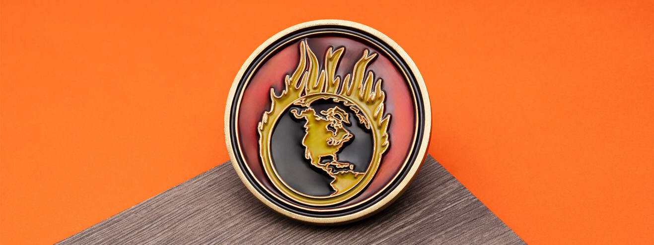Bronze coin with a gold globe ringed in flames over red and black translucent enamel, on dark wood and orange paper