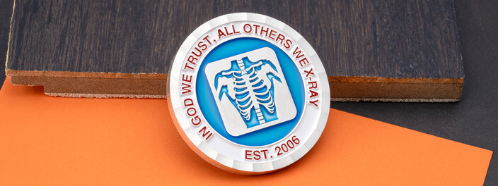 Silver coin with a blue x-ray of a ribcage and red lettering reading In God We Trust, All Others We X-Ray