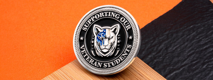 Silver rope edged coin with a mountain lion head in flag colors, ringed by Supporting Our Veteran Students